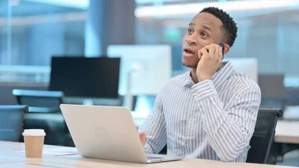 Afrikanischer Geschäftsmann mit Laptop im Smartphone-Gespräch — Stockfoto