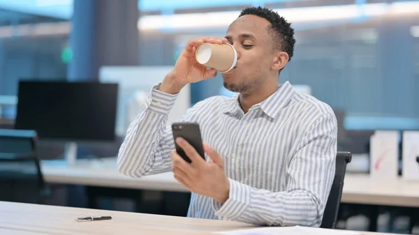 Empresário Africano usando Smartphone e Beber Café — Fotografia de Stock