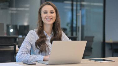 Genç İş Kadını Bilgisayarda çalışırken Kameraya Gülümsüyor
