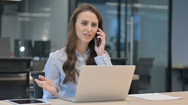 怒っているビジネスマン女性ノートパソコンを使用している間スマートフォンで話す — ストック写真