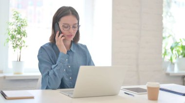 Dizüstü bilgisayarı olan ve akıllı telefondan konuşan kadın. 