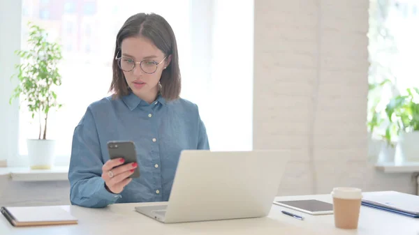 Mujer con ordenador portátil Navegación por Internet en el teléfono inteligente en el trabajo —  Fotos de Stock