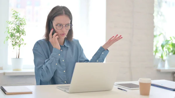Розлючена жінка з ноутбуком розмовляє на смартфоні — стокове фото