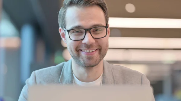 Primer plano de hombre joven con el ordenador portátil sonriendo a la cámara — Foto de Stock