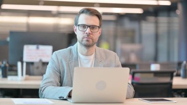 Ofiste dizüstü bilgisayar kullanırken Genç Adam Kameraya Bakıyor