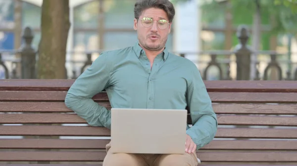 Людина, яка повертається до болю, користуючись ноутбуком на відкритому повітрі — стокове фото