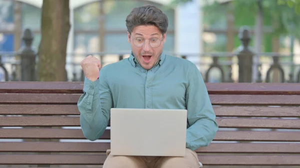 Homme Célébration tout en utilisant ordinateur portable en plein air sur banc — Photo