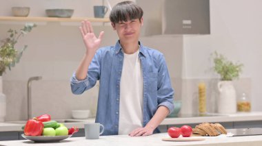 Genç Asyalı adam mutfakta dikilirken görüntülü arama yapıyor.