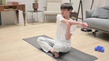 Genç Asyalı adam evde esneme hareketleri yapıyor.