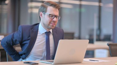 Dizüstü bilgisayarı olan genç bir iş adamı ofiste sırt ağrısı çekiyor. 