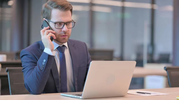 Ung affärsman med bärbar dator talar på telefon — Stockfoto