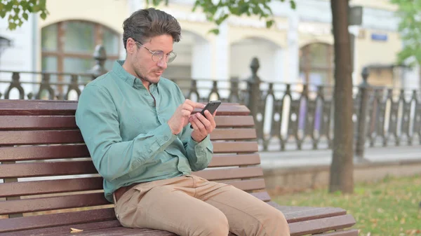 Reifer erwachsener Mann surft auf Smartphone im Sitzen auf Parkbank — Stockfoto