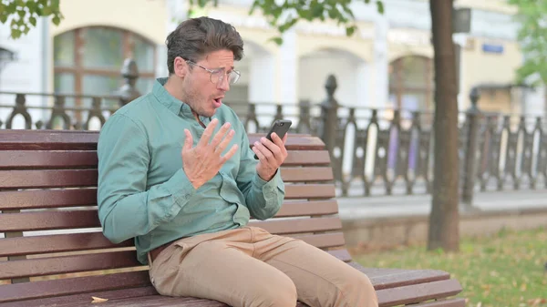 坐在长椅上的成年男子在智能手机上有故障 — 图库照片