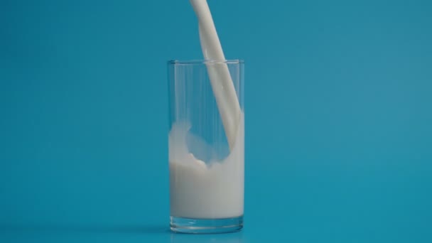 Movimento lento de derramamento de leite em vidro, fundo azul — Vídeo de Stock