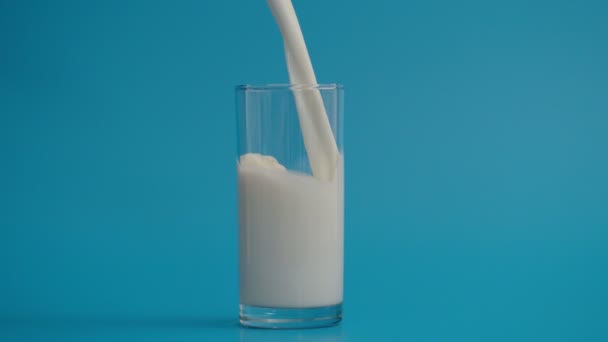 Αργή κίνηση της χύνοντας γάλα σε γυαλί, μπλε φόντο — Αρχείο Βίντεο