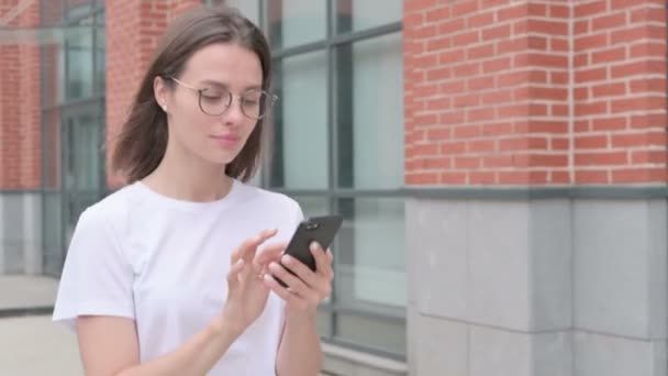 Молодая женщина во время прогулки по улице просматривает Интернет — стоковое видео