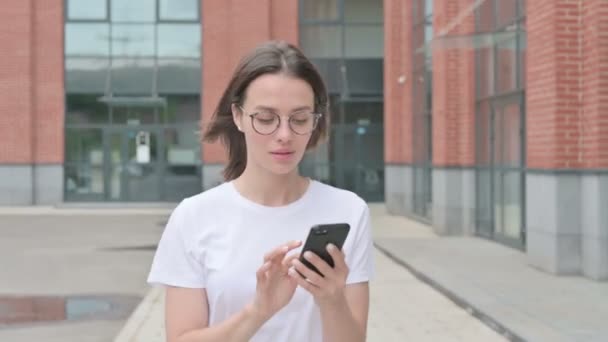 Молодая женщина празднует на смартфоне во время прогулки по улице — стоковое видео
