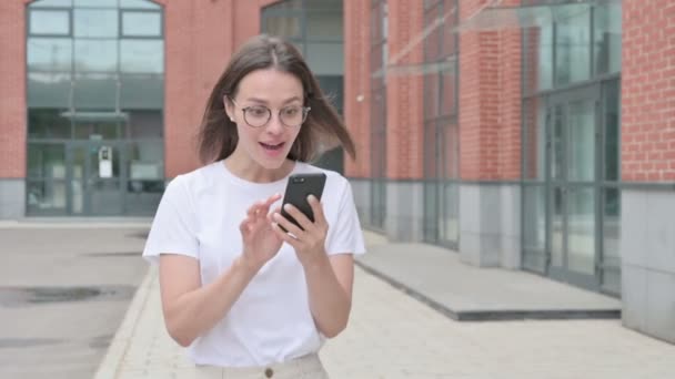 Młoda kobieta świętuje sukces na smartfonie podczas spaceru po ulicy — Wideo stockowe