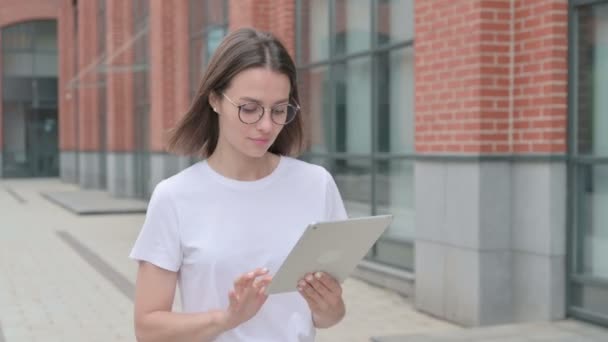 Mujer joven trabajando en la tableta mientras camina por la calle — Vídeo de stock