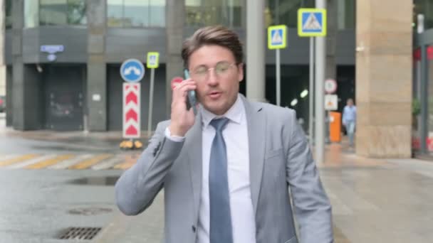 Podnikatel mluví na telefonu při chůzi po ulici — Stock video