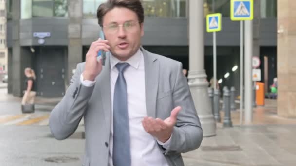 Podnikatel mluví na telefonu zlostně při chůzi po ulici — Stock video