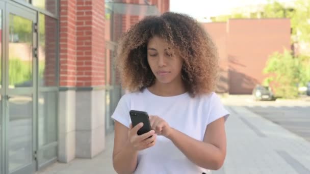 外を歩いている間にスマートフォンで損失に反応するアフリカの女性 — ストック動画