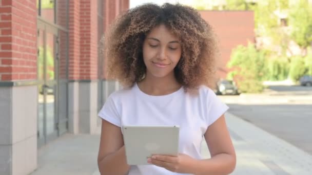 Mujer africana joven navegando por Internet en la tableta mientras camina fuera — Vídeos de Stock