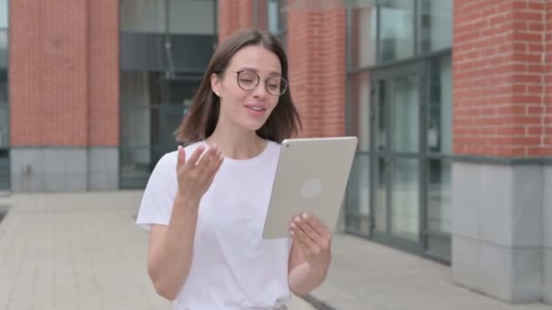 Mujer joven haciendo videollamada en la tableta mientras camina por la calle — Vídeos de Stock