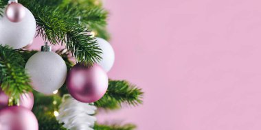 Beyaz ve pembe mevsimlik ağaç süsüsüyle süslenmiş Noel ağacıyla süslenmiş bir pankart. Pembe arka planda boş kopya alanı ile süslenmiş.