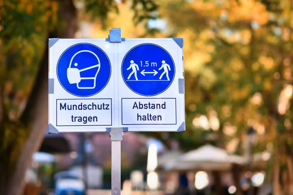 Signs for face mask and distance requirement in German city center with text saying \'wear facial mask\' and \'keep distance\'