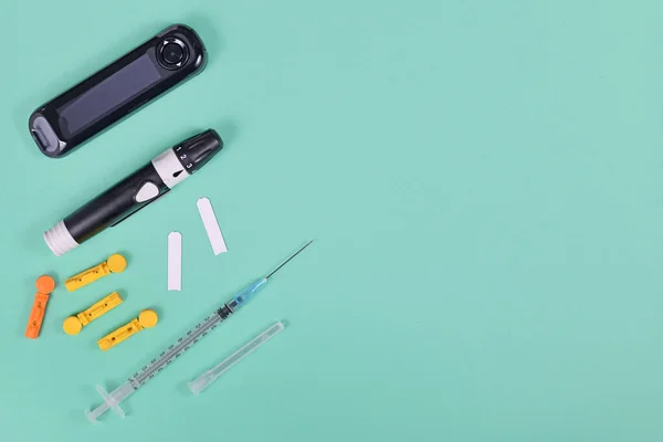 Tools for diabetes treatment with blood glucose sugar meter, lancets, test strips, syringe and lancing device on green background with copy space