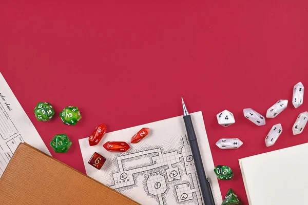 Tabletop role playing flat lay with RPG game dices, hand drawn dungeon map, rule books and pen at bottom of red background with empty copy space