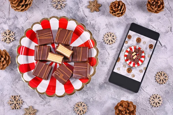 Concept for food photography with German layered winter cake pralines called \'Baumkuchen\' on plate next to mobile phone with picture taken of food