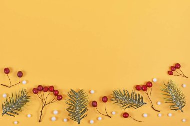 Mevsimlik kırmızı kış meyveleri, beyaz kartopları ve köknar dalları sarı arka planda boş kopya alanı ile