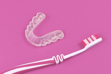 Özelleştirilmiş şeffaf diş ısırığı önleyici pembe arka planda diş fırçasıyla alt çene hizalayıcıları