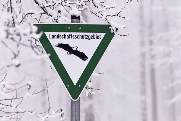 Green sign with eagle for German Nature Reserve, a category of protected area within Germany\'s Federal Nature Conservation Act in snow forest