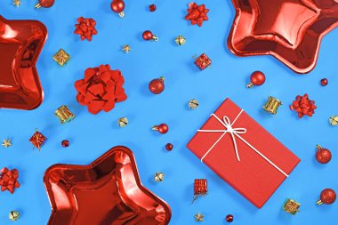 Noel düz nükteli kırmızı yıldız şekilli kağıt parti tabakları, ağaç süslemeleri, hediye kutusu ve kurdeleler, mavi arka planda yıldızlar ve çanlar.