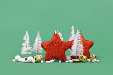 Yıldız şeklinde kırmızı ağaçlar, beyaz Noel ağaçları, altın çanlar ve yeşil arkaplanda kartopu süslemeleri.