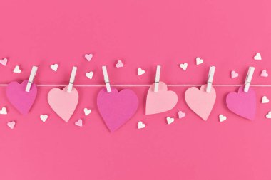 Sevgililer Günü arkaplanı pembe kağıt kalplerle askıdan sarkan şeker parçacıklarıyla