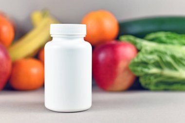 Meyve ve sebzelerin önündeki bulanık arka planda gıda takviyesi şişesi