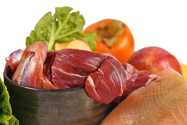 Close up of dog bowl with mixture of biologically appropriate raw food containing meat chunks, fish, fruits and vegetables isolated on white background