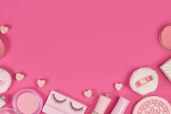 Cute makeup beauty products like brushes, face powder or lipsticks surrounding pink background with empty copy space