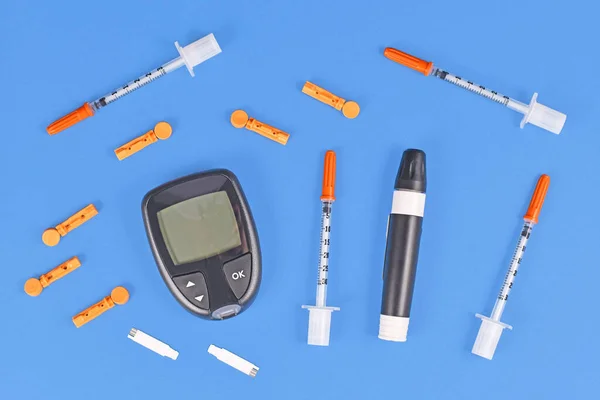 Diabetes treatment equipment with blood glucose sugar meter, lancets, syringes and lancing device on blue background