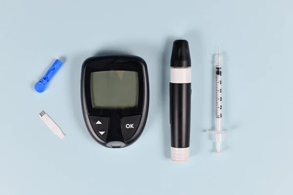 Diabetes treatment equipment with blood glucose sugar meter, lancet, syringe and lancing device on blue background