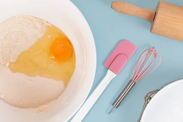 Preparing dough for shortcrust cake base with flour, sugar, baking bowder and egg in mixing bowl next to kitchen utensils