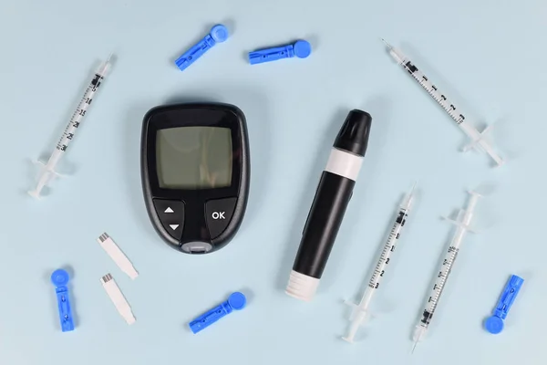 Equipment for Diabetes treatment with blood glucose sugar meter, lancets, syringes and lancing device on blue background