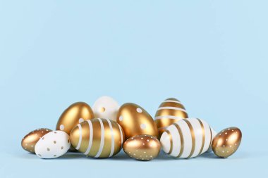 Zarif altın ve beyaz Paskalya yumurtaları mavi arka planda basit noktalar ve çizgiler ile boyanmış.