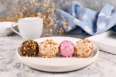 Beyaz, pembe ve kahverengi çikolata kaplı renkli küçük kek topları beyaz tabağa serpiştirilmiş.