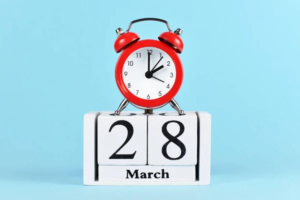 Time change for daylight saving summer time in Europe on March 28th concept with red alarm clock and calendar on blue background