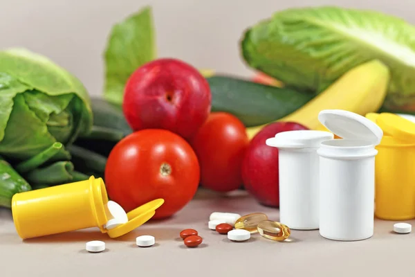 Bottles with pills of food nutrition supplements in front of fruits and vegetables in background